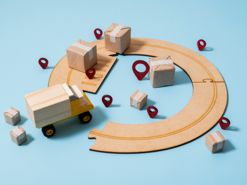 pequeno caminhão de madeira com caixas e pinos de marcação de mapa, representando o supply chain